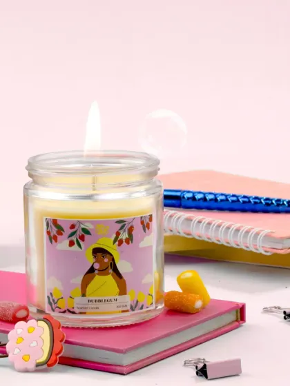 A sweet and simple setup for a bubblegum candle, styled on a stack of pink notebooks with cute hair clips and candy. This image evokes a sense of youthful nostalgia and cozy study sessions.