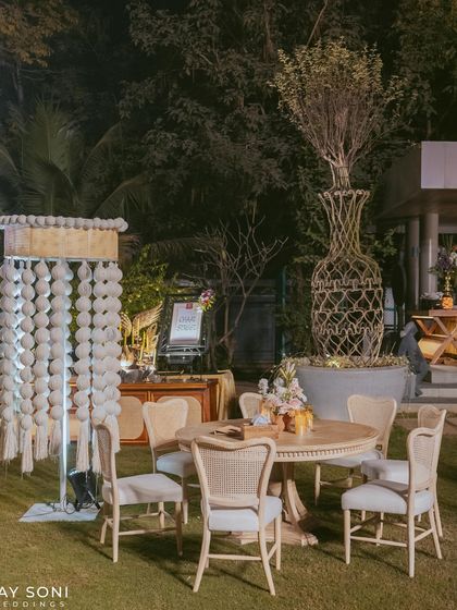 A cozy seating arrangement for an outdoor wedding, featuring classic cane-back chairs around a wooden table, complemented by unique decor elements like a macrame lamp.