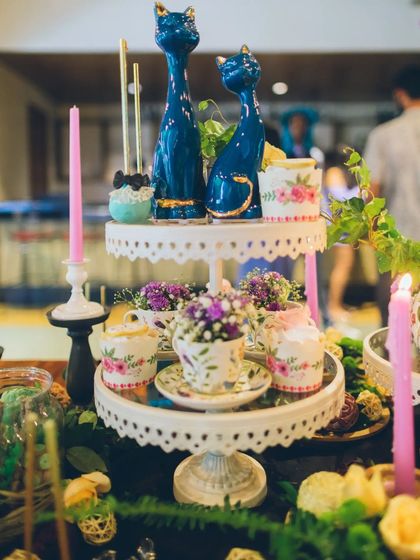 Details on the two-tiered dessert stand, showcasing quirky cat figurines alongside floral-patterned teacups and candles. Each element was carefully chosen to contribute to the whimsical, storybook atmosphere.
