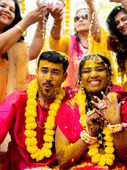 A close-up of the couple, covered in haldi and flowers, with huge smiles on their faces.