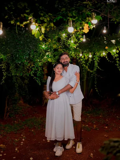 A romantic embrace under trees adorned with hanging light bulbs. This simple yet beautiful setup creates a magical, intimate feel for night shoots.