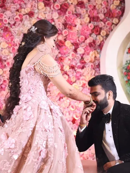 An intimate and classic moment from a ring ceremony. The groom gently kisses the bride's hand against a beautiful wall of pink flowers, a simple gesture full of love and promise. This is the kind of timeless, emotional still photograph that becomes a cherished memory.