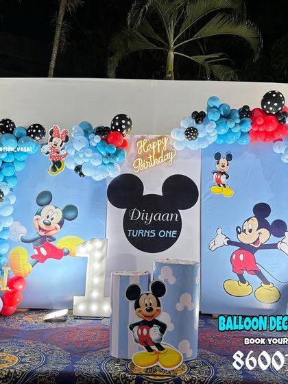 Diyaan's first birthday with a classic Mickey Mouse theme. The setup includes a custom backdrop, character cutouts, and a balloon arrangement in Mickey's signature red, blue, and black colors.