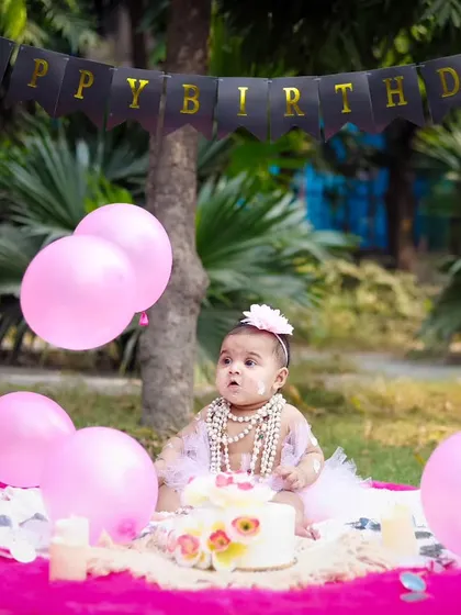 A wide shot of the outdoor cake smash setup, with pink balloons and a 'Happy Birthday' banner creating a festive scene.