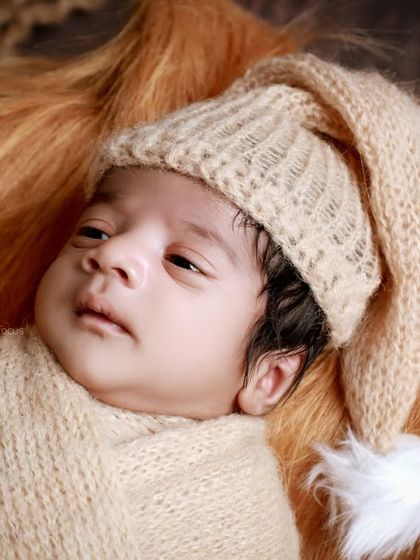 An awake baby in a knit pixie hat, looking curious. The warm, ginger-colored fur provides a beautiful and soft base for the portrait.