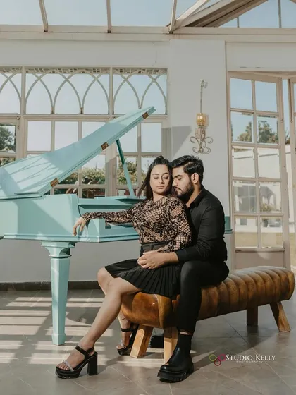 An elegant pre-wedding shot by a piano. The makeup is sophisticated and chic, matching the classic black outfits and the refined setting of the shoot.