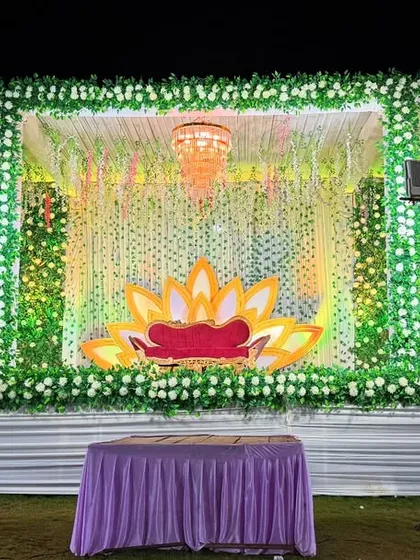 A fresh and natural stage design with a frame covered in white flowers and greenery. The lotus-shaped seating adds a unique, traditional touch.
