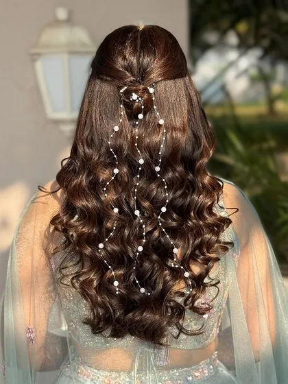 A beautiful half-up hairstyle with soft curls and a delicate pearl hair accessory cascading down the back. This look is dreamy and ethereal.