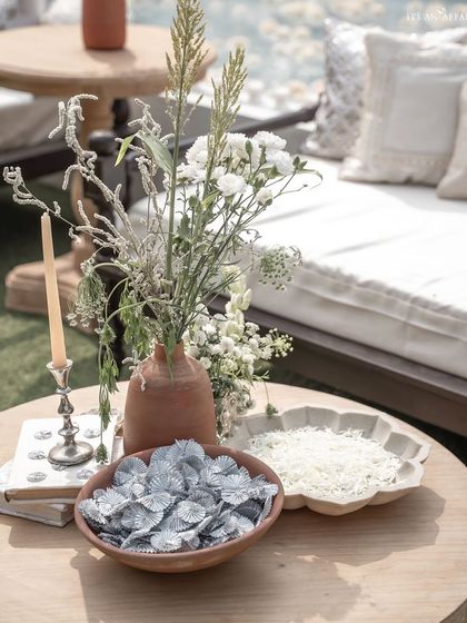 A detail shot showing bowls of flower petals for guests to shower, alongside rustic terracotta vases and modern silver candlesticks.