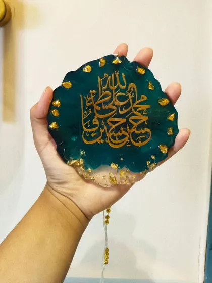 A custom car hanging featuring Panjatan names in gold calligraphy on a deep teal resin base, decorated with gold leaf.