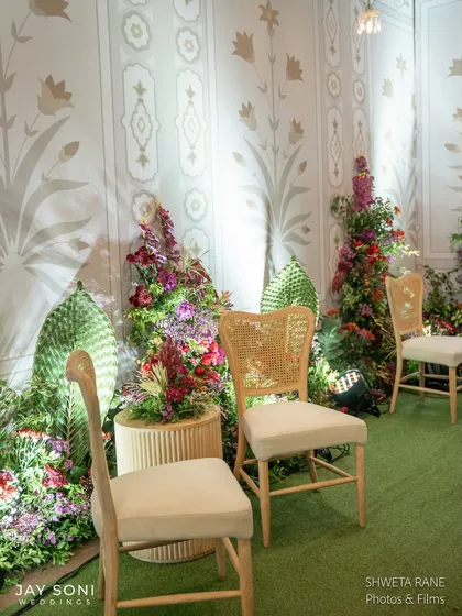 Simple yet elegant seating at the entrance, with classic wooden chairs and cane details placed against a backdrop of lush florals and decorative wall panels.