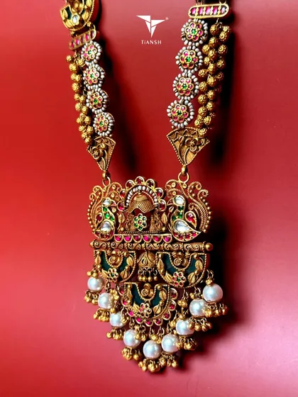 Some pieces do not just sit on your skin, they become a part of you. This handcrafted 22K gold temple necklace is adorned with intricate motifs of divine figures, delicate pearls, and vibrant kundan stones, making it a regal statement for any grand occasion.