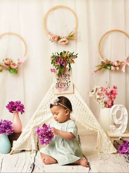 A nine-month milestone session with a lovely boho-floral theme. The baby girl explores the purple flowers in front of a lace teepee.