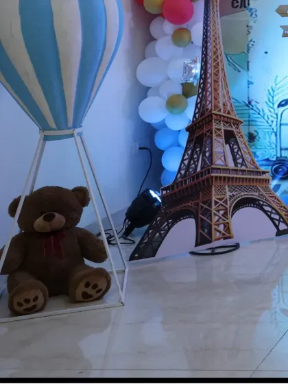 A close-up of the teddy bear in a hot air balloon basket next to the Eiffel Tower prop.