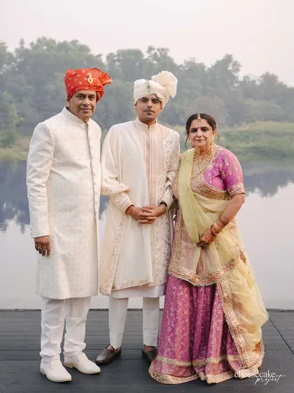 A groom with his parents by the lake. His serene cream and pink sherwani, inspired by Koyalia birds, was crafted with over 80 hours of hand embroidery to match the wedding's tranquil theme.