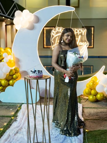 A full-length shot of the birthday girl enjoying her special celebration, holding a bouquet of flowers in front of the moon decor.