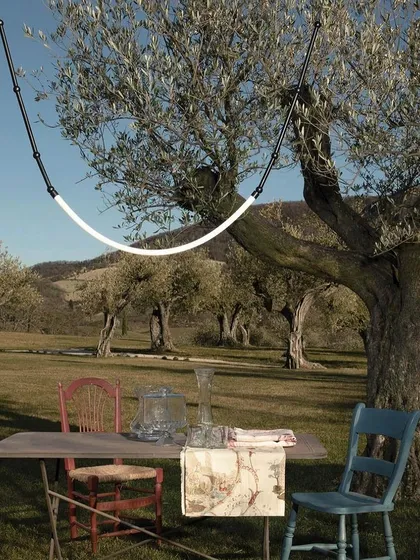 The Leda outdoor light hung between trees, illuminating a rustic picnic table. This flexible system allows you to bring beautiful, high-design lighting to any part of your property.