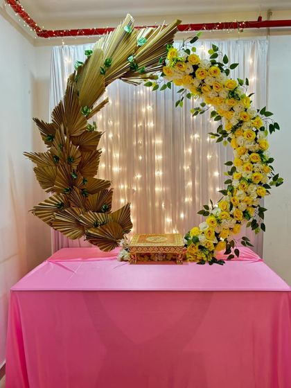 A modern and artistic crescent moon arch for a Ganpati or Navratri setup. One side features yellow and white roses, while the other is made of golden dried palm leaves, creating a beautiful contrast.
