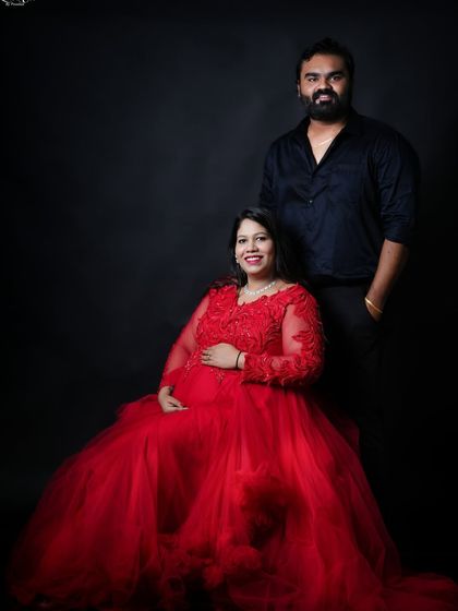 A classic seated portrait of the couple. The woman's stunning red gown is the centerpiece, while her partner stands beside her, creating a formal and elegant composition.