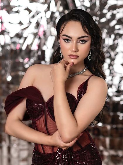 A modern party look with sharp, winged eyeliner and a sequined dress. The shiny, metallic backdrop enhances the glamour and makes the image pop.