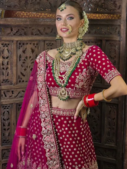 A model wearing a beautiful pink velvet lehenga with gold embroidery. This is a classic bridal choice, available for rent along with the matching jewellery.