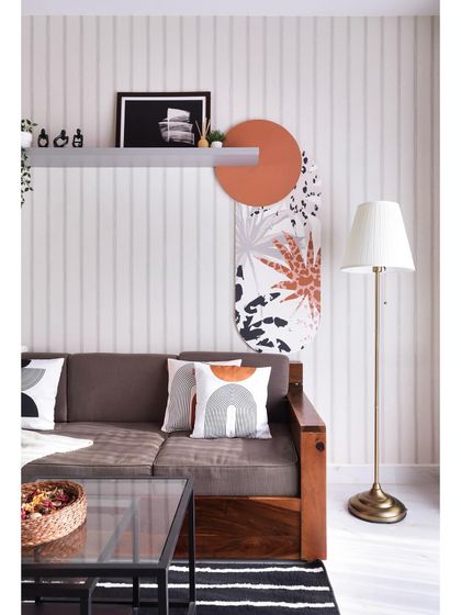 This living area showcases a blend of textures and patterns. The striped wallpaper provides a neutral backdrop for the solid wood sofa, while abstract art and geometric cushions add a contemporary, artistic touch.