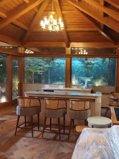 The finished gazebo interior, where the warmth of wooden elegance meets a statement chandelier. Cozy rattan accent chairs and a bar area create the perfect space to unwind.