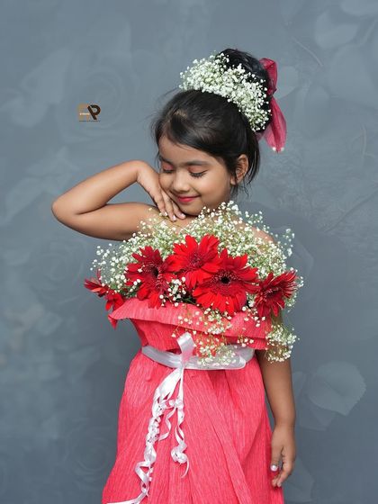 A close-up of the girl in the flower dress, smiling sweetly. The combination of red gerberas and baby's breath creates a stunning and unique look.