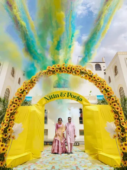 A spectacular Haldi ceremony entrance, with the couple framed by a sunflower arch and vibrant color smoke. We love capturing the energy and joy of pre-wedding festivities.