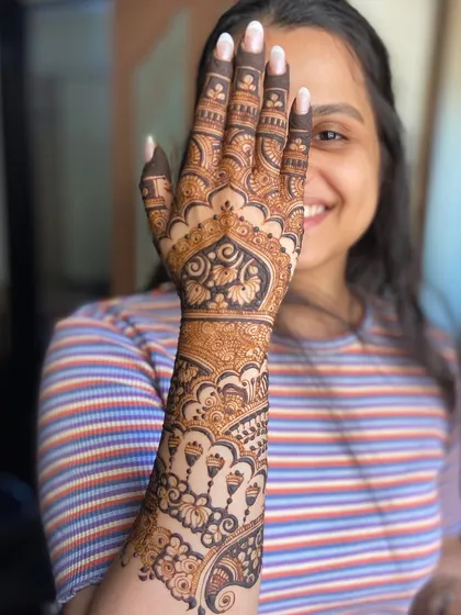 A smiling client showing off her detailed engagement mehendi.