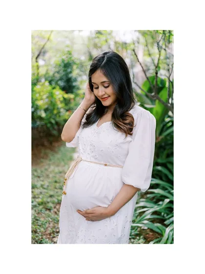 A classic solo maternity portrait in a lush, green setting. The mother-to-be gently holds her bump, looking down with a soft smile, a timeless pose that is always beautiful.