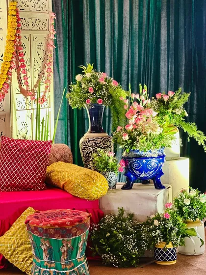 Detailing of a Mehendi corner with colorful printed stools, bright cushions, and elegant floral arrangements in traditional blue and white pottery.