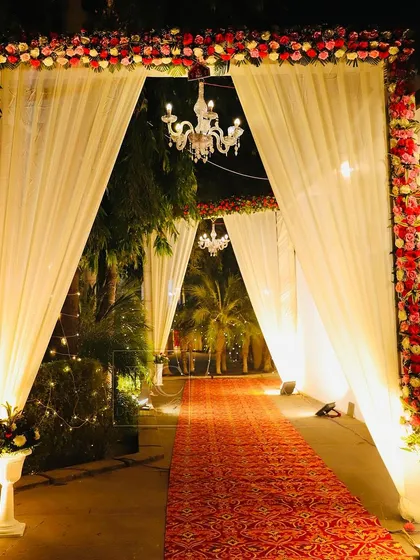 A classic and romantic wedding entrance. I designed a tunnel of arches draped in white fabric, framed with red and white flowers, and lit by beautiful chandeliers.