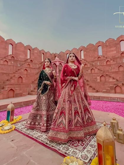Two brides, one royal vision. Showcasing two of my most exquisite bridal lehengas, one in deep green and the other in classic red, perfect for a grand wedding ceremony.