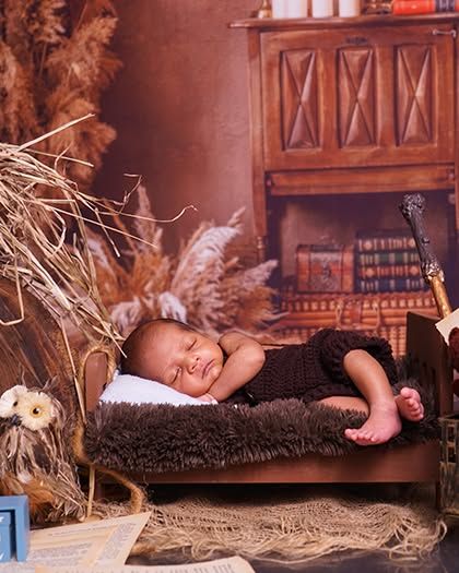 A wider view of the rustic setup, showing the baby sleeping on a tiny bed with an owl prop and a library backdrop. It’s a complete story in one frame.