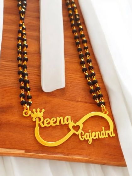 This infinity-style name pendant combines two names with a crown and heart detail, all on a mangalsutra chain. It’s a design that blends modern symbolism with traditional elements.