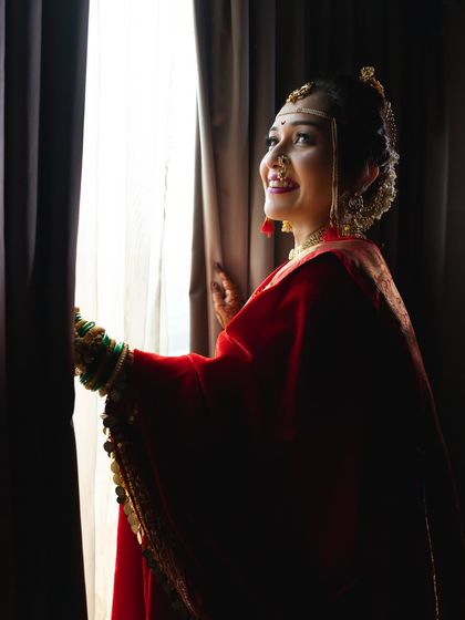 A bride peeks through the curtains, her face lit with a happy, expectant smile.