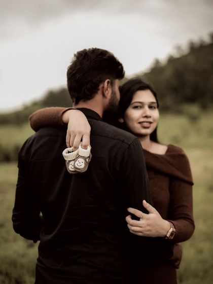 A playful over the shoulder shot. The mom-to-be looks back with a smile while holding a pair of baby shoes, a subtle and sweet pregnancy announcement.