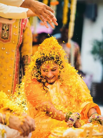 A beautiful shot of the bride being showered with flower petals during her Haldi ceremony. Her happy expression shows the joy of being surrounded by loved ones.