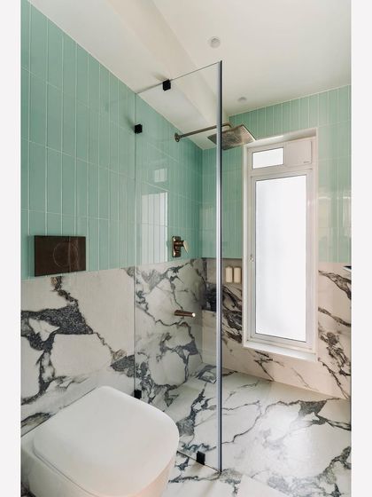 The master bathroom in the Plush Abode project is arrayed with Statuario tiles and mint green subway tiles. This creates an interesting contrast with the brushed gold finished bathroom fittings, for a look of pure elegance.