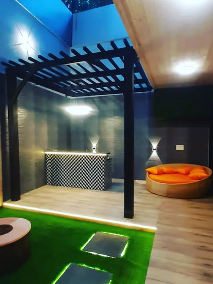 A cozy indoor-outdoor space featuring a small pergola over a bar, with a comfortable lounge seat nearby.