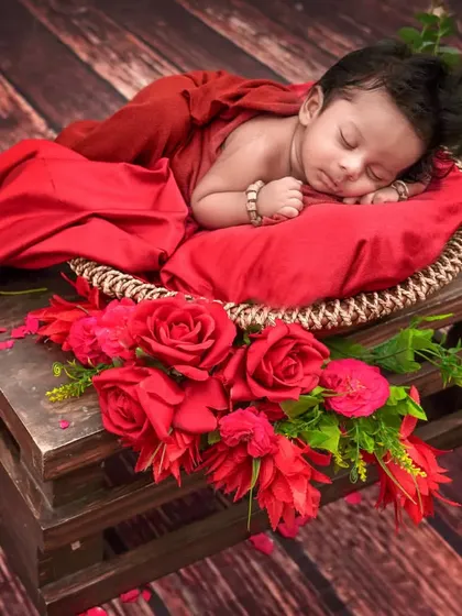 A baby sleeps on a red pillow atop a wooden crate, surrounded by beautiful red roses for a bold and classic look.