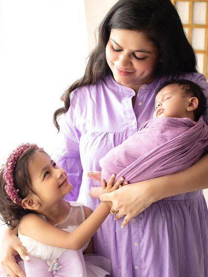 A beautiful moment as an older sister gazes lovingly at her new baby sibling, held securely in their mother's arms.