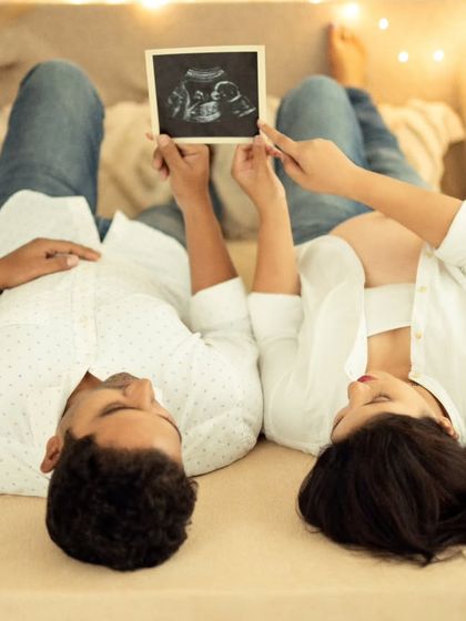 A unique perspective from above, showing the couple lying down and holding their sonogram picture together.