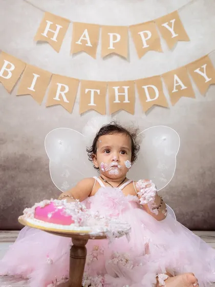 A full portrait of a baby girl dressed as a fairy, completely covered in pink frosting during her very first cake smash.