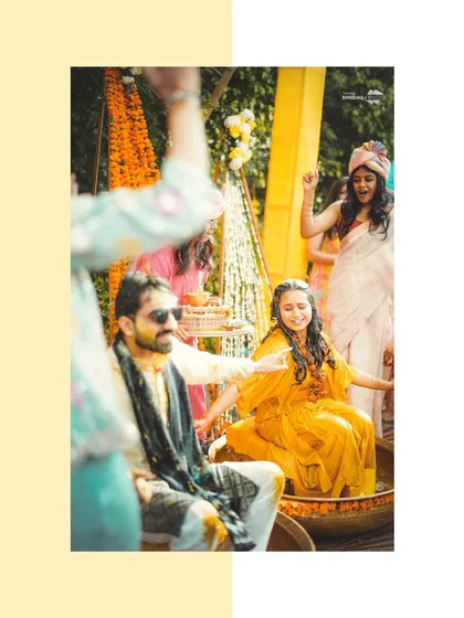 A candid moment from a Haldi ceremony. The bride and groom are all smiles as they get covered in turmeric, surrounded by their cheering friends and family.