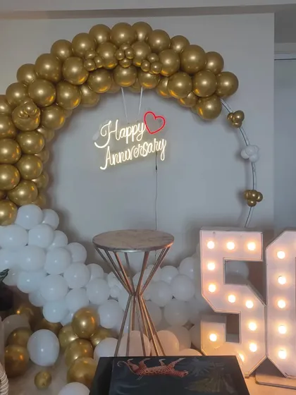 Celebrating a golden 50th anniversary with a beautiful white and gold balloon ring, a neon sign, and large marquee '50' numbers.