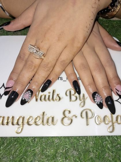 A chic black nail set with a pink accent nail featuring an abstract line design and a beautiful pearl flower embellishment.