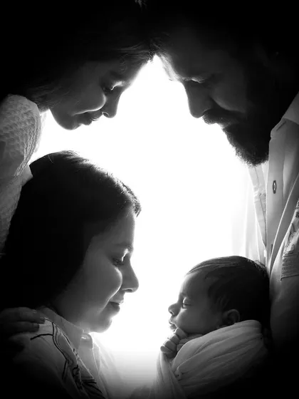 A powerful black and white silhouette of a family encircling their newborn, highlighting their bond and love.