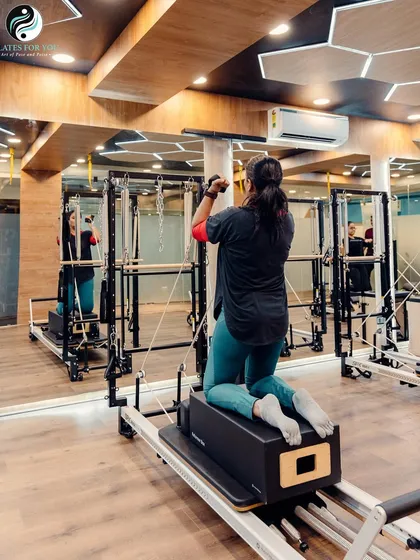 Here, a client uses the reformer box and arm straps on the Cadillac tower. This setup allows for targeted upper body work while maintaining core stability.